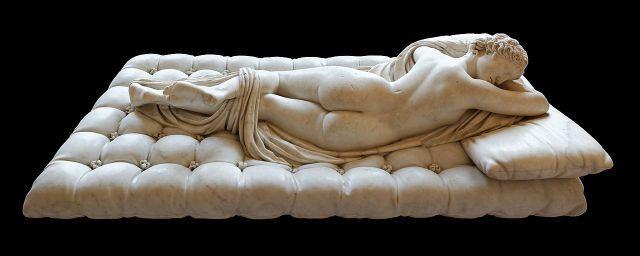 Photograph of the Hermaphroditus Borgehese or Sleeping Hermaphroditus. The photo shows the sculpture's backside, with round buttocks, a somewhat unisex hairstyle of a top bow that is worn by both Aphrodite and Apollo, and a beautiful arched back. One leg is lifted, entangled in a blanket or himation.