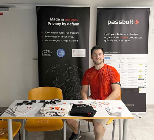 Passbolt booth at Pass the Salt 2025 in Lille, with a team member seated behind a table of swag.