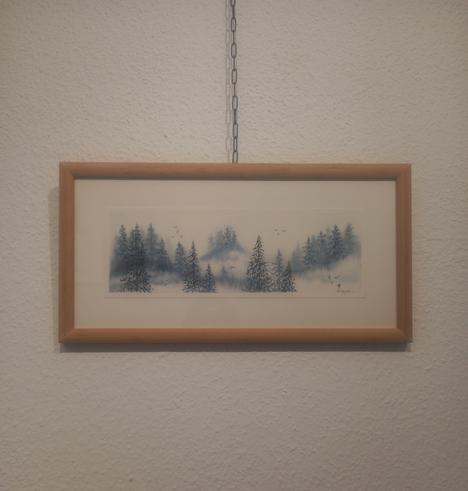 Foto a una ilustración apaisada enmarcada y colgada en la pared. Está hecha en acuarelas monocromática y representa un pinar sobre tres montes. 