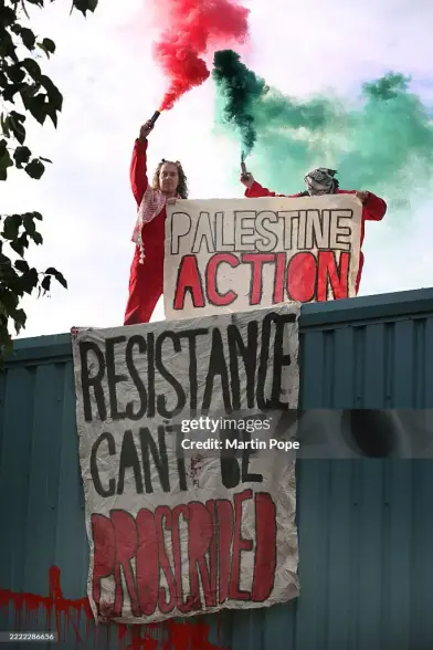 Image Two occupiers in red overalls hold a Palestine Action banner and a red flare and a green flare while occupying the roof of the Guardtech building in Brandon UK 🇬🇧 The company is in business with Israeli Defence contractor Elbit Systems 

Banner 1 text:
P A L E S T I N E  
   A C T I O N 

Banner 2 text: 
R E S I S T A N C E 
  C A N ‘ T   B E
P R O S C R I B E D