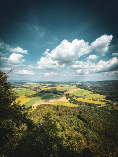 Widok z punktu widokowego umieszczonego na szczycie góry stołowej. Poniżej, pola, lasy , odległy horyzont. 