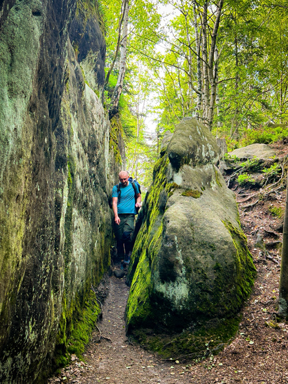 Kompan włóczęgi idący wąską ścieżką, przeciskający się pomiędzy skałami. Dookoła świerkowy, gęsty las. 