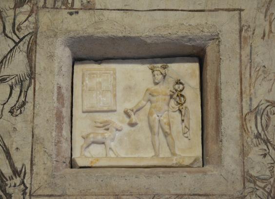 Bas-relief of Hermes and a ram. The god is in the nude, wearing only his iconic winged petasos hat and a himation draped over his left arm. He holds his kerykeion staff (caduceus in Latin) in his left and a money purse in his right. An object that looks like a modern window is in the top left corner above the ram.