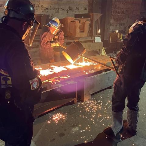 Zwei Männer gießen flüssiges Metall aus dem Schmelztiegel in Formen