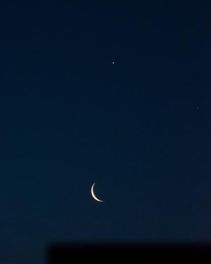 La luna, Venus y Saturno en una alineación que recuerda una cara sonriente, siendo los planetas los dos ojos y la luna la boca. El cielo está oscuro y empieza a amanecer.
