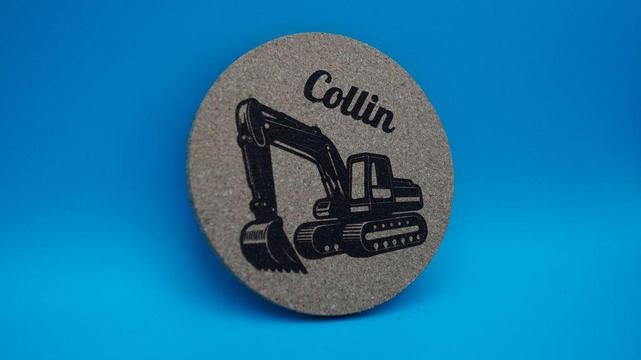 Runder Korkuntersetzer mit detailreich graviertem Bagger und dem Namen „Collin“ darüber.