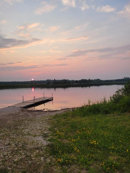 Small dock at boat launch with sunset and sun reflected in water.
