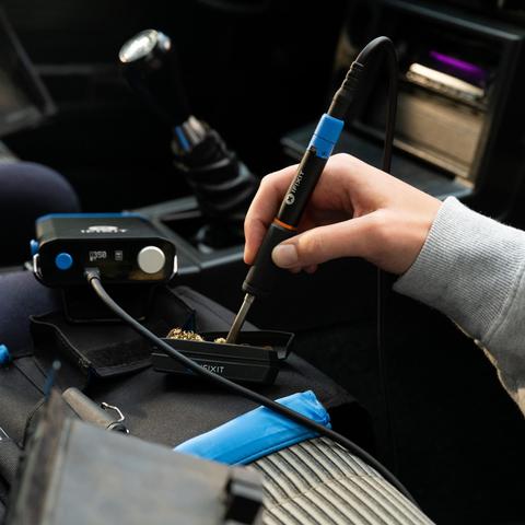 Close-up of an iFixit soldering iron being cleaned in brass wool on the front seat of a car.