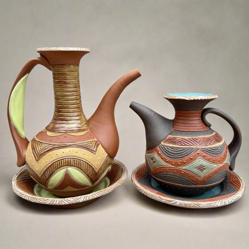 The two ewers facing each other, the taller orange one on the left and the shorter black one on the right. The different spout heights create an interesting negative space between the two objects.