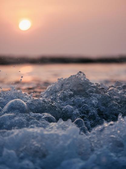 Close up of a crashing and foaming ocean wave against the setting sun in the background.