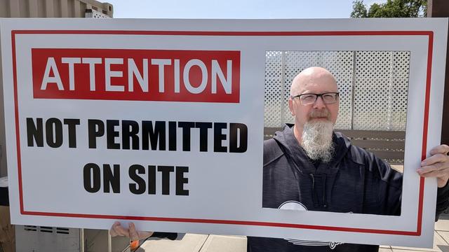 Scott holding a sign that says Attention: Not Permitted