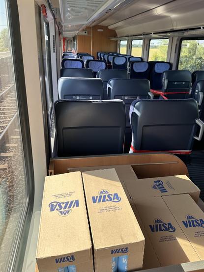 Interior of a train showing empty rows of seats and boxes of mineral water on a table.