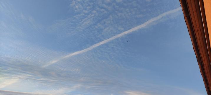 Un avion traverse un ciel bleu strié de nuages fins et réguliers, laissant une longue traînée blanche qui coupe l’image en diagonale