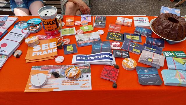 Infomaterial & Seenotrettungssticker auf einer orangen Tischdecke.