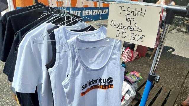 Tops & T-Shirts an einer Kleiderstange.
Das vorderste ist mit solidarity and Résistance und dem Seebrücke FFM Logo