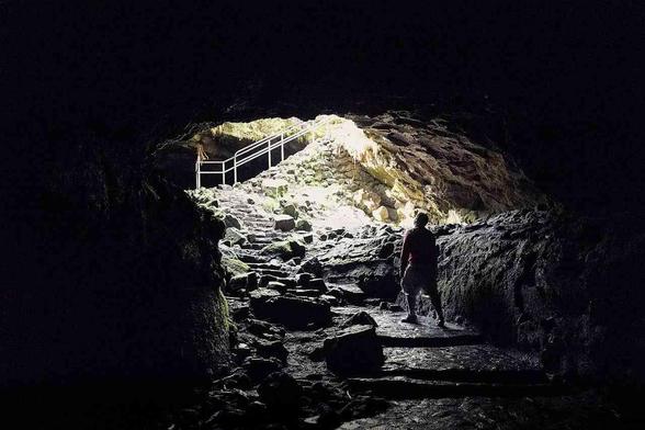 Inside a dark cave, steps leading upward to a light source, with a person walking toward the opening.