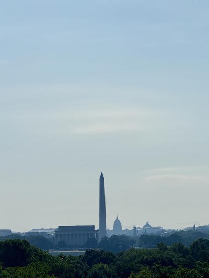 A picture of the monuments in Washington DC as seen from across the river at the Netherlands Carillon in Arlington. There’s a fair bit of haze under mostly blue skies. 