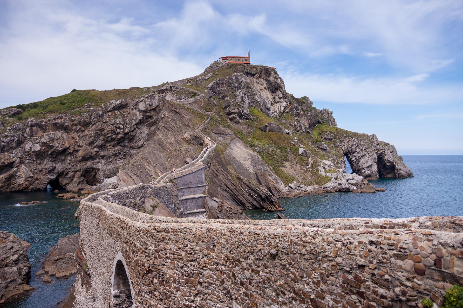 Un puente estrecho, de piedra, que cruza una pequeña franja de mar hasta llegar a un islote y subir zigzagueando hasta la pequeña ermita que hay en la cima. Cielo azul con nubes blancas (un típico día de verano). Un puente estrecho, de piedra, que cruza una pequeña franja de mar hasta llegar a un islote y subir zigzagueando hasta la pequeña ermita que hay en la cima. Cielo azul con nubes blancas (un típico día de verano).