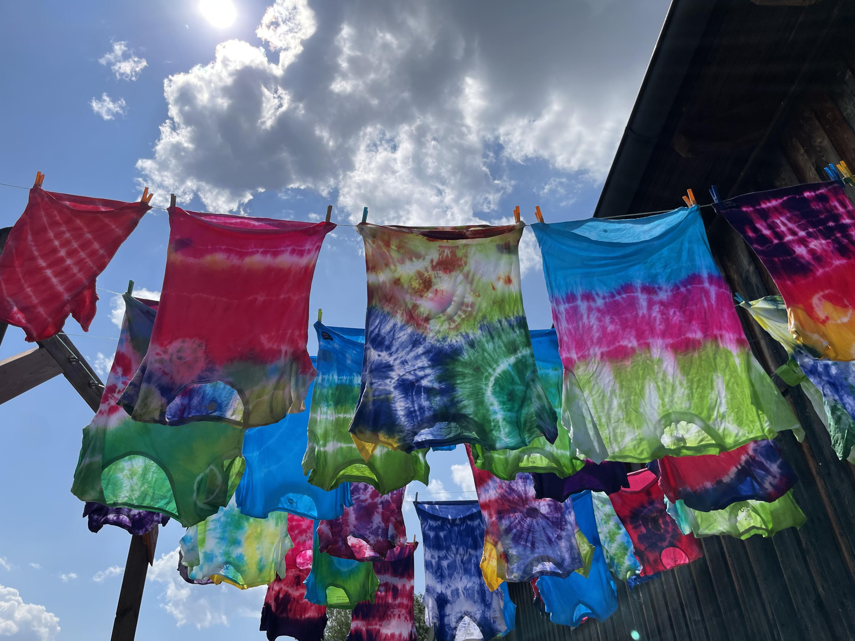 Bunte frisch gebatikte Shirts hängen zum Trocknen auf der Wäscheleine. Die Sonne steht dahinter und bringt die Farben zum Leuchten Bunte frisch gebatikte Shirts hängen zum Trocknen auf der Wäscheleine. Die Sonne steht dahinter und bringt die Farben zum Leuchten