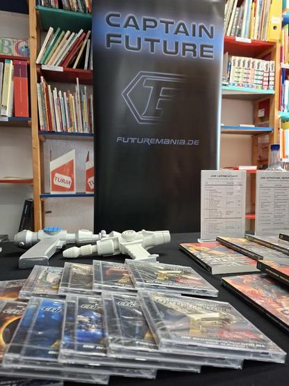 Das Foto zeigt das Futuremania-Rollup vor einem der zahlreichen Bücherregale im 1. UG der Phantastischen Bibliothek Wetzlar. Im Vordergrund, auf dem Tisch davor, liegen linkerhand die Captain-Future-Hörspiele aus dem Maritimverlag und rechterhand die CF-Neuübersetzungen aus dem Golkonda-Verlag, dahinter zwei Protonenpistolen ;-)