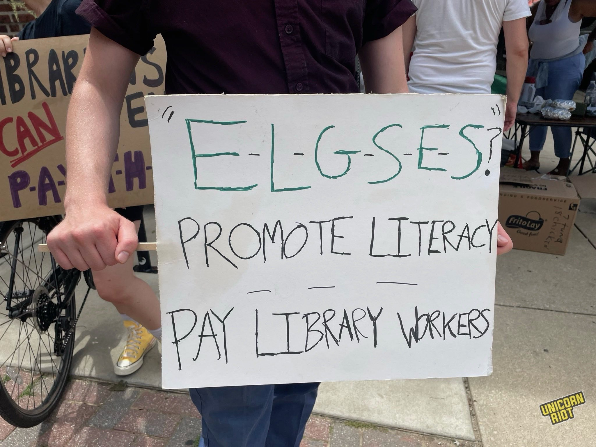 picket sign reads "E-L-G_S-E-S?" "Promote Literacy - Pay Library Workers" in reference to Mayor Parker's infamous Super Bowl gaffe