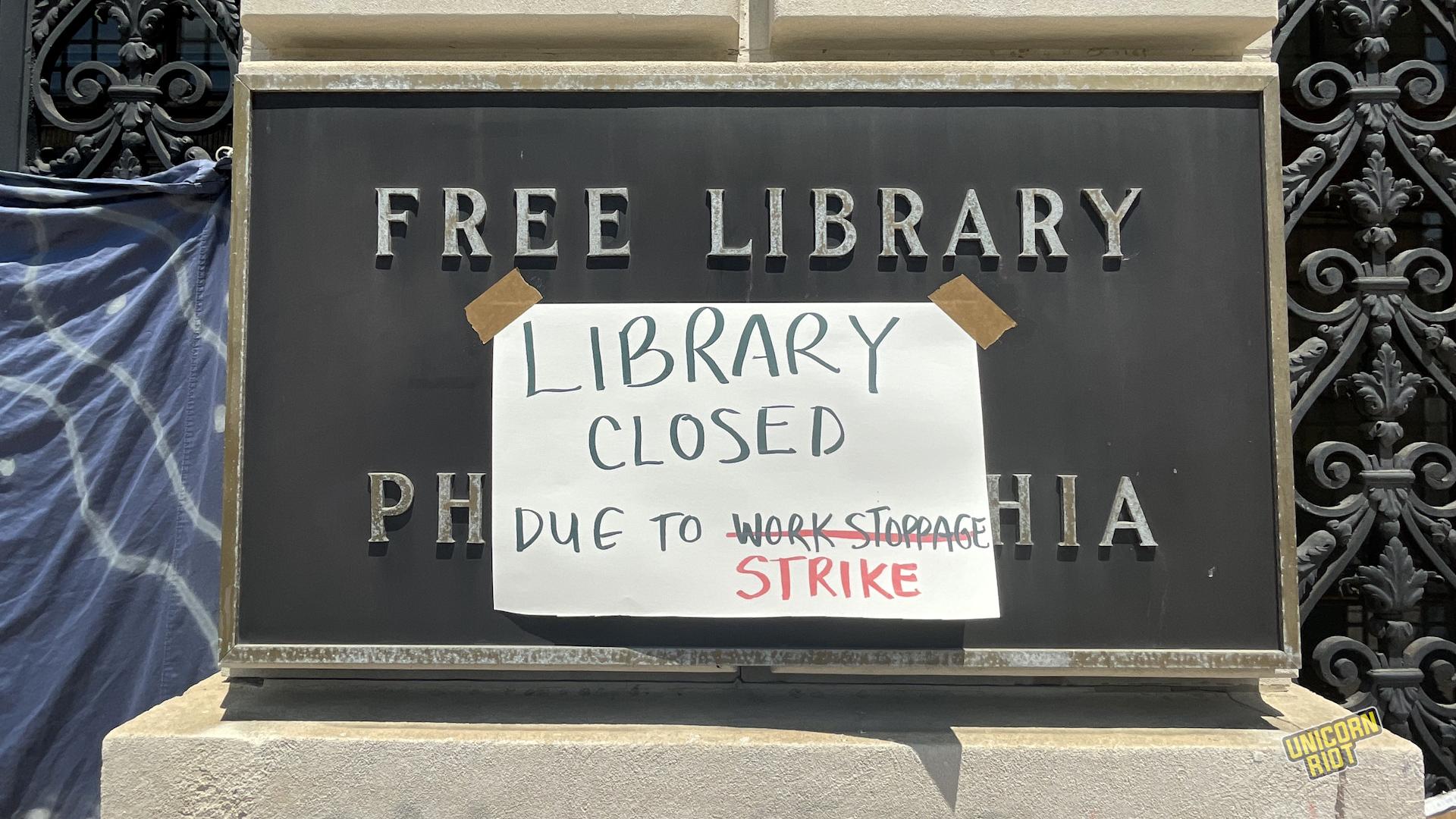 "Library closed due to work stoppage" with "work stoppage" crossed out and replaced with "strike" written on a piece of paper taped over a "FREE LIBRARY OF PHILADELPHIA" plaque by the entrance to the main Parkway branch of the library