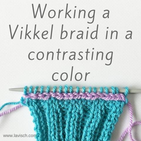 A turquoise swatch in 2x2 rib, on top of which a Vikkel braid in a lilac yarn is visible, just beneath the knitting needle. The live stitches on the needle are in the turquoise yarn.