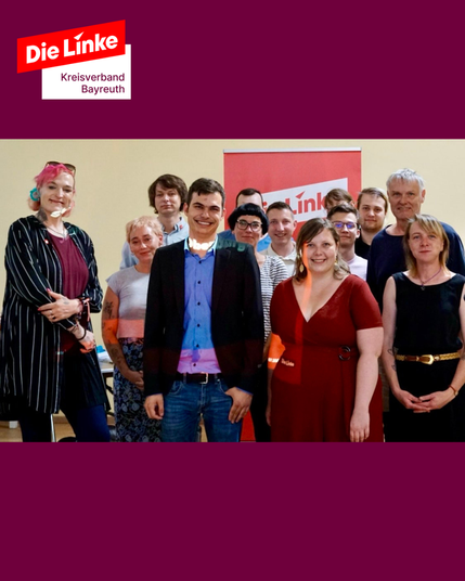 Gruppenfoto mit allen an diesem Tag gewählten Kandidierenden von Die Linke Bayreuth – Stadtratsliste, Kreistagsliste sowie Oberbürgermeister- und Landratskandidatur. Etwa 13 Personen stehen vor einem roten Die-Linke-Rollup und blicken in die Kamera. In der Mitte: Jannick Metz und Juliane Glaschke. Alle wirken fröhlich und entschlossen.

