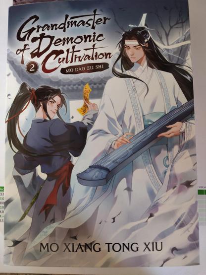 Cover Grandmaster of Demonic Cultivation Band 2, die beiden Hauptfiguren , einer in weiß mit einem Musikinstrument in der Hand, der andere in Schwarz mit einem Talisman