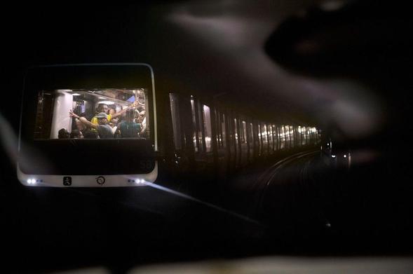 Street photography of a Paris metro train in a tunnel, viewed through the window reflection of another metro train, with passengers visible inside.