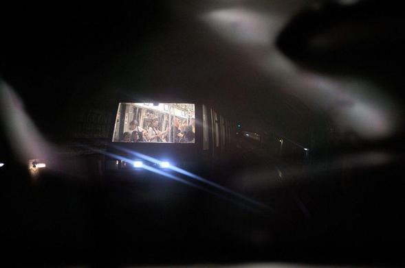 Street photography of a Paris metro train in a tunnel, viewed through the window reflection of another metro train, with passengers visible inside.