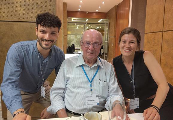 Alessandro Innocenti und Adriana Sacristán-Martín mit dem Chemie-Nobelpreisträger Johann Deisenhofer (Mitte). Auf dem Bild zu sehen sind sitzend an einem Tisch ein älterer Herr im hellen Hemd in der Mitte, rechts neben ihm eine junge Frau mit einem schwarzen Oberteil und links neben ihm ein junger Mann im hellblauen Hemd (Foto: privat) 