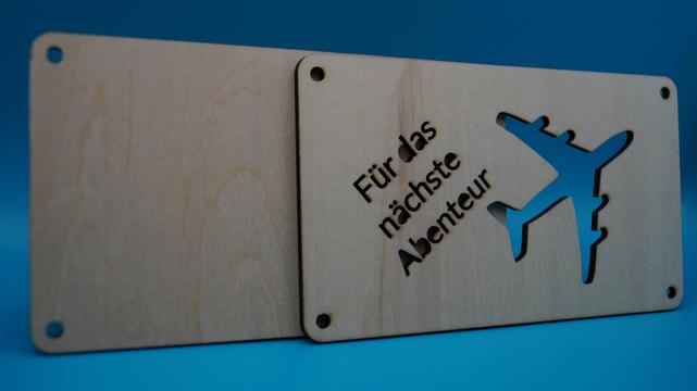 Zweiteilige Holzkonstruktion mit ausgestanztem Flugzeugmotiv, seitlich geöffnet, zur Vorbereitung des Geldgeschenks
