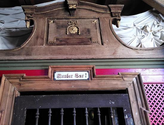 Eine Art antikes, altarartiges Holztor, auf dem „Wunder Bar!“ steht.