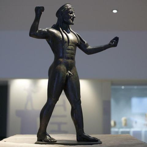 A bronze statue of Zeus striding forward, his arm raised to hurl a thunderbolt now missing. He has long, braided hair and a crown.