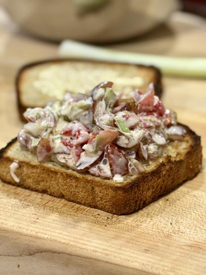 A sandwich on a cutting board piled with tomatoes, green onions, and a tomato water mayonnaise. 