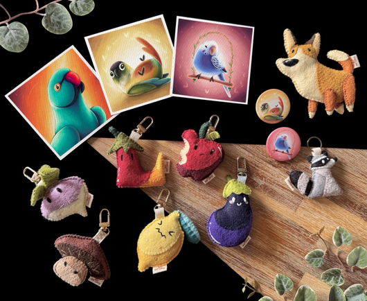 Picture of new products set to release on my website tomorrow: 3 mini prints featuring an Indian ringneck, a green cheek conure, and a budgies two button badges matching the motive of the conure and budgie prints; a small corgi felt plushie; a raccoon keychain; and 6 fruits and vegetable themed bag charms! 
