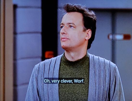 Star Trek The Next Generation scene. Q (an otherwise normal human looking guy) is standing on the bridge of the Enterprise D. He's wearing a grey robe and green undershirt. He's talking to someone off screen. (It's Worf)
Closed caption reads, "Oh, very clever, Worf. Eat any good books lately?"