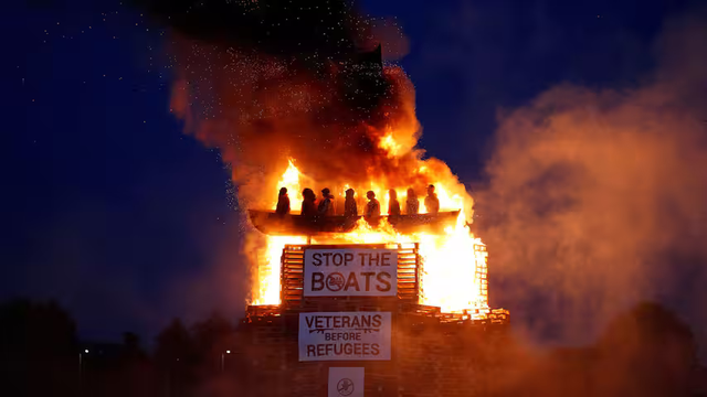 Picture of a boat on fire with refugee dolls on board. 
