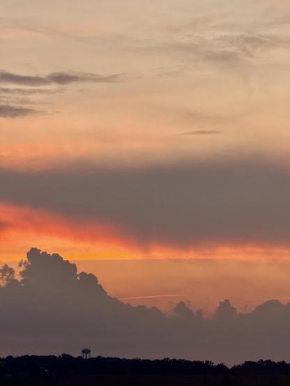 A fiery sunset behind some interesting clouds. There’s a water tower to the left of the image in the distance 