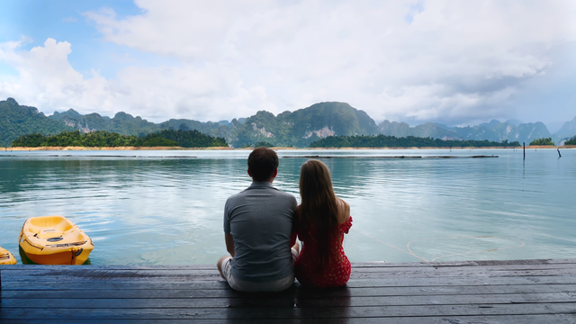Couple sitting next to each on a dock overlooking a bay and mountains in the distance.