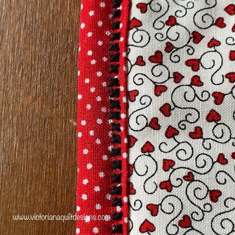 A row of black cross stitches, along the edge of red with white polka dot fabric. 