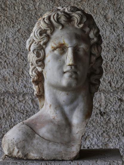 Marble bust of the god Helios. His left shoulder is missing. He has curly hair and there are holes that were used for the attachment of a sun-ray crown.