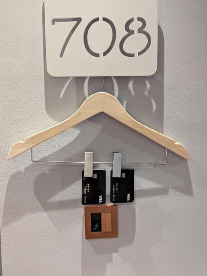 Pants hangar hung beneath a hotel room sign. Clipped to the hangar are namecards resembling payment cards with the Visa logo, fake chip, and inscription "not an infosec furry".