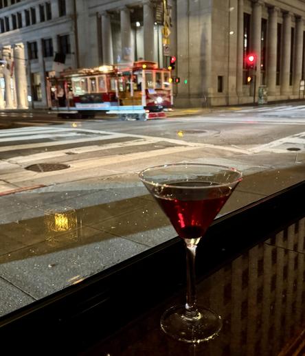 Picture of a Manhattan cocktail on a window ledge with a cable car passing by in the background.