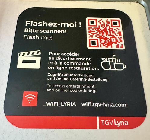 Kleber auf dem Tischchen am Platz. Zeigt einen 3D-Barcode und dreisprachig:
Flashez-moi!
Bitte scannen!
Flash me!