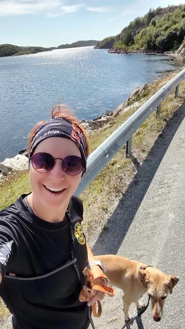 Selfie von Ylvi und mir. Ich trage Laufkleidung und Sonnenbrille. Im Hintergrund die Leitplanke einer Straße, das Meer und felsige Hügel.