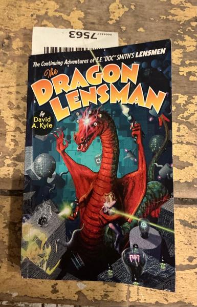 A book with a long red dragon holding a ray gun on a hand attached to a wing and a woman firing a ray gun in a hand tied to another arm with vacuum tube electronics around him.  Title reads: "The Continuing Adventures of E.E. DOC SMITH'S LENSMEN",  The DRAGON LENSMAN by David A. Kyle