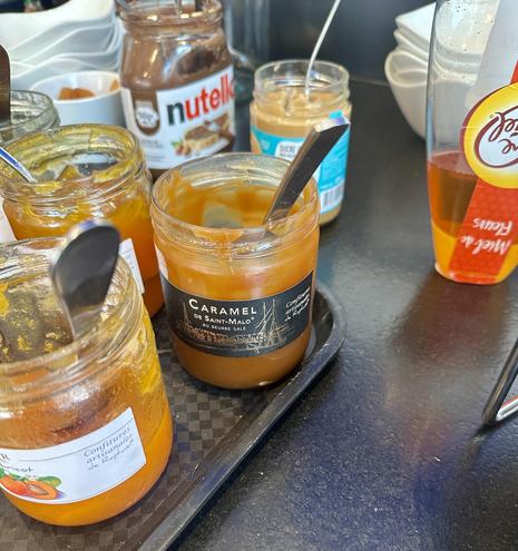 Auf einem Tablett stehen mehrere Marmeladengläser. Das in der Mitte ist beschriftet mit «Caramel de St-Malo au Beurre salé». Ein Löffel steht im Glas, das nur noch leicht gefüllt ist.