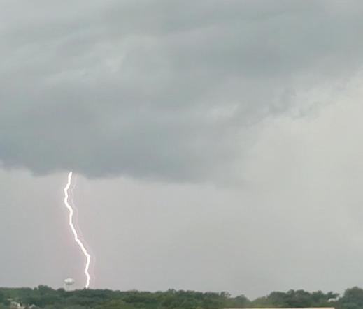 A lightning bolt strikes the ground in the distance near a water tower 